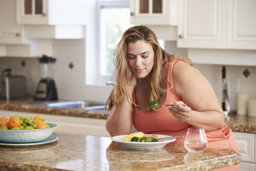 33515003 - overweight woman eating healthy meal in kitchen
